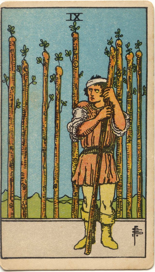 Nine of Wands: The bandaged head, the sideways glance, the wand held close, the palisade of eight wands. Rider–Waite–Smith tarot, 1909.